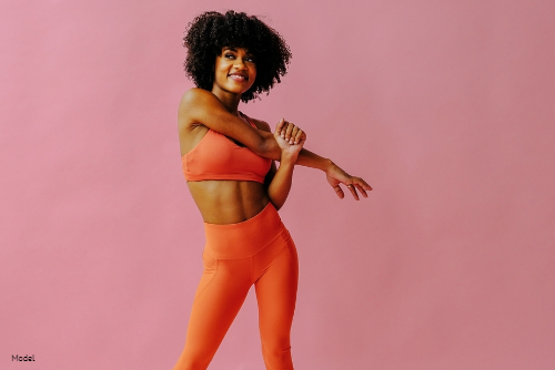 Confident woman in orange leggings and sports bra stretching her arm