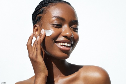Confident woman with clear, bright skin applying a skin care product to her cheek while smiling