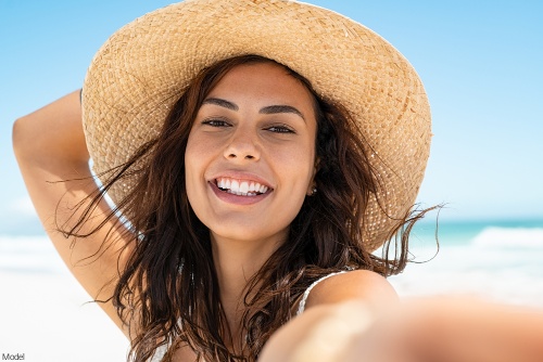 Joyful woman with clear skin wearing a straw sun hat at the beach smiling