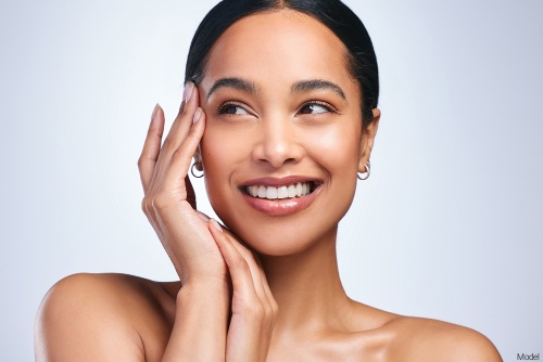 Joyful woman with clear, bright skin smiling and gently touching her temple