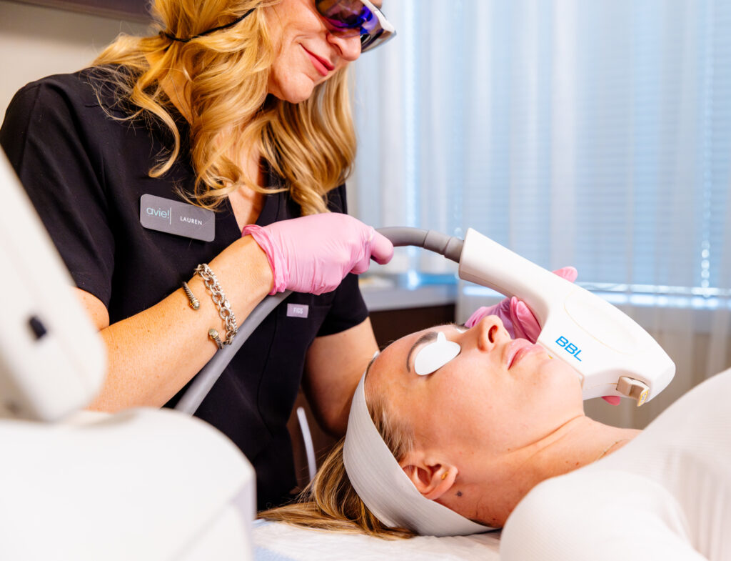 Provider wearing protective eyewear and gloves places the BBL HEROic device on patient's face as the patient lays back. This is a light-based skin tightening treatment in Loudoun County.