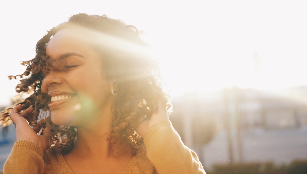 Girl standing in the sunlight smiling and feeling confident after getting a treatment for Emface in Loudoun County