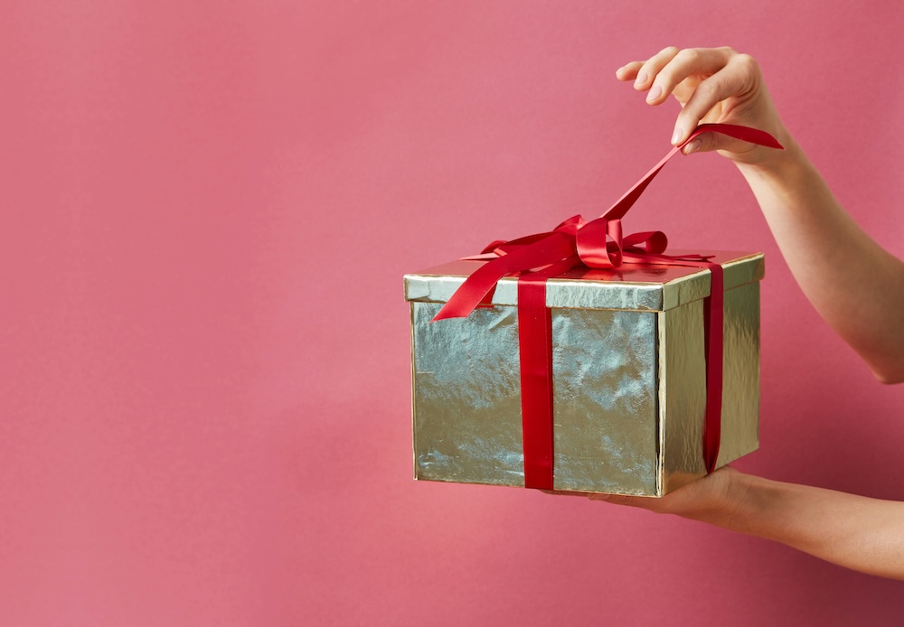 Person holding a present neatly wrapped with a bow on top. They are holding one of the strings, ready to open it and reveal what is inside—which could be a gift card to Avie! Med Spa + Laser Center to receive a Facial Laser Treatment in Loudoun County.
